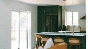 A modern kitchen with a central island, bar stools, and a dining area with a sofa. - Cozy Cabin Getaway (St. Ignace)