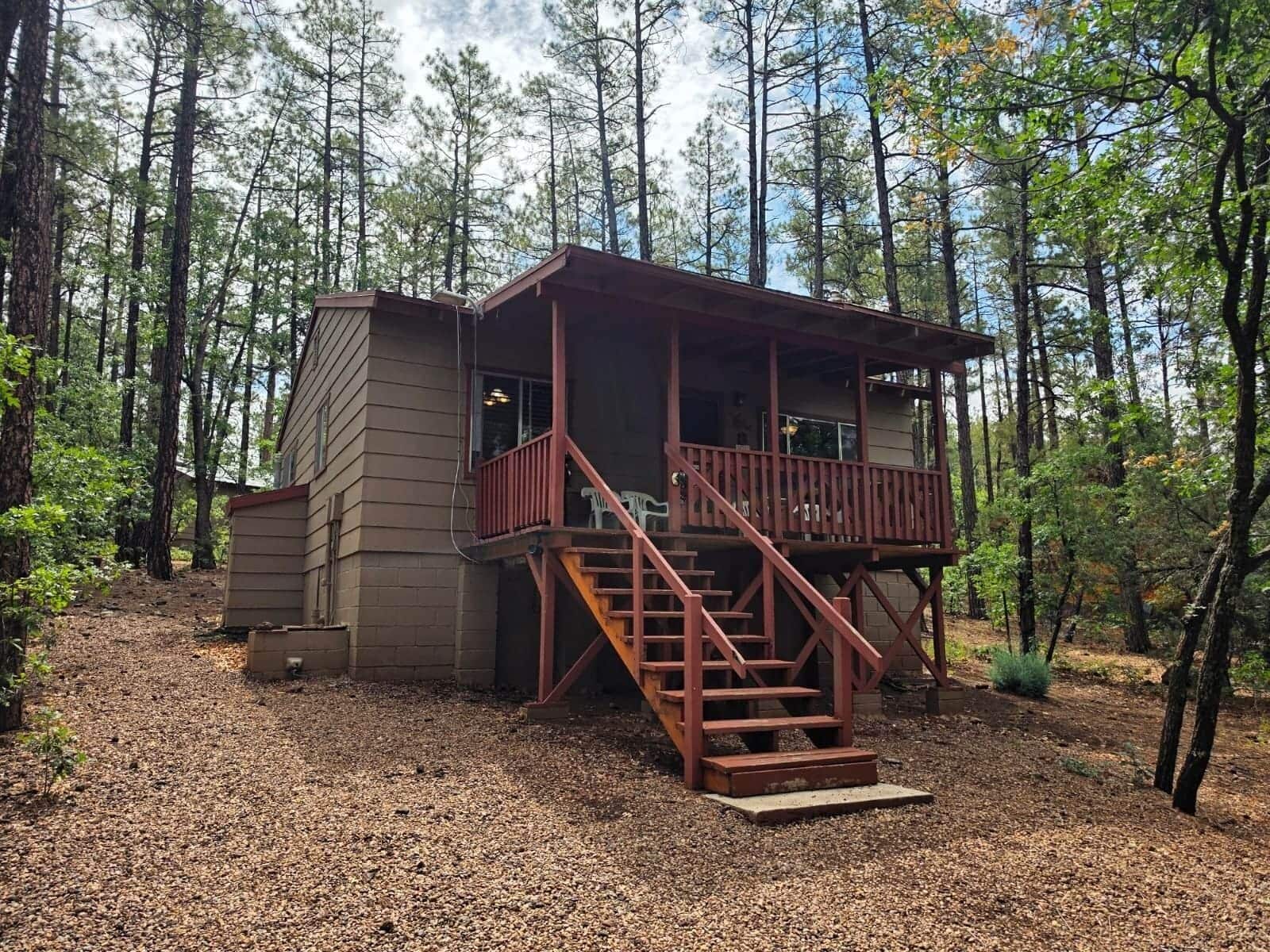 Eine Holzhütte mit einer Holzterrasse und einer Treppe zu einem Balkon, umgeben von einem Wald.