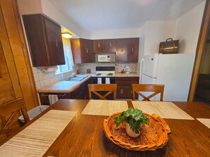 A kitchen with wooden cabinets, a microwave, stove, and a refrigerator. There is a dining table with chairs and a woven basket with a plant.