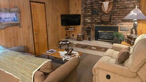 A cozy living room with wooden paneling, a fireplace, a television, and a comfortable seating area. - Northwoods (#9) Cabin in the Pines (Pinetop-Lakeside)