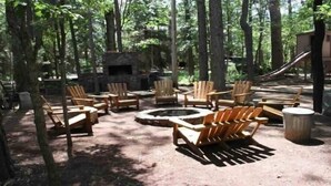 Un espace extérieur boisé avec un foyer en pierre entouré de fauteuils Adirondack en bois.