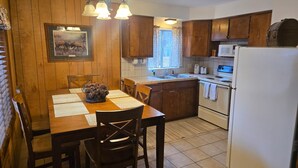 Une cuisine avec des meubles en bois, une table à manger avec des chaises, un lustre, un four à micro-ondes et un réfrigérateur.