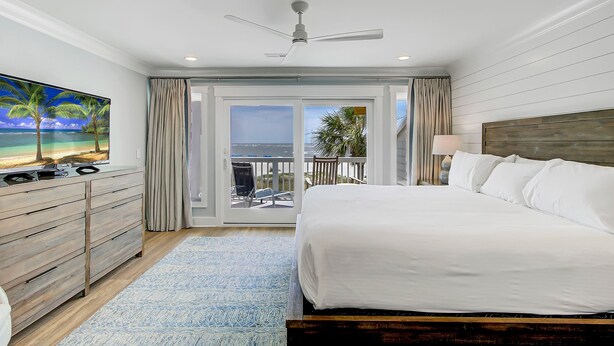 Ein Schlafzimmer mit einem großen Bett, einem Deckenventilator, einem Fernseher auf einer Kommode und einem Balkon mit Blick.