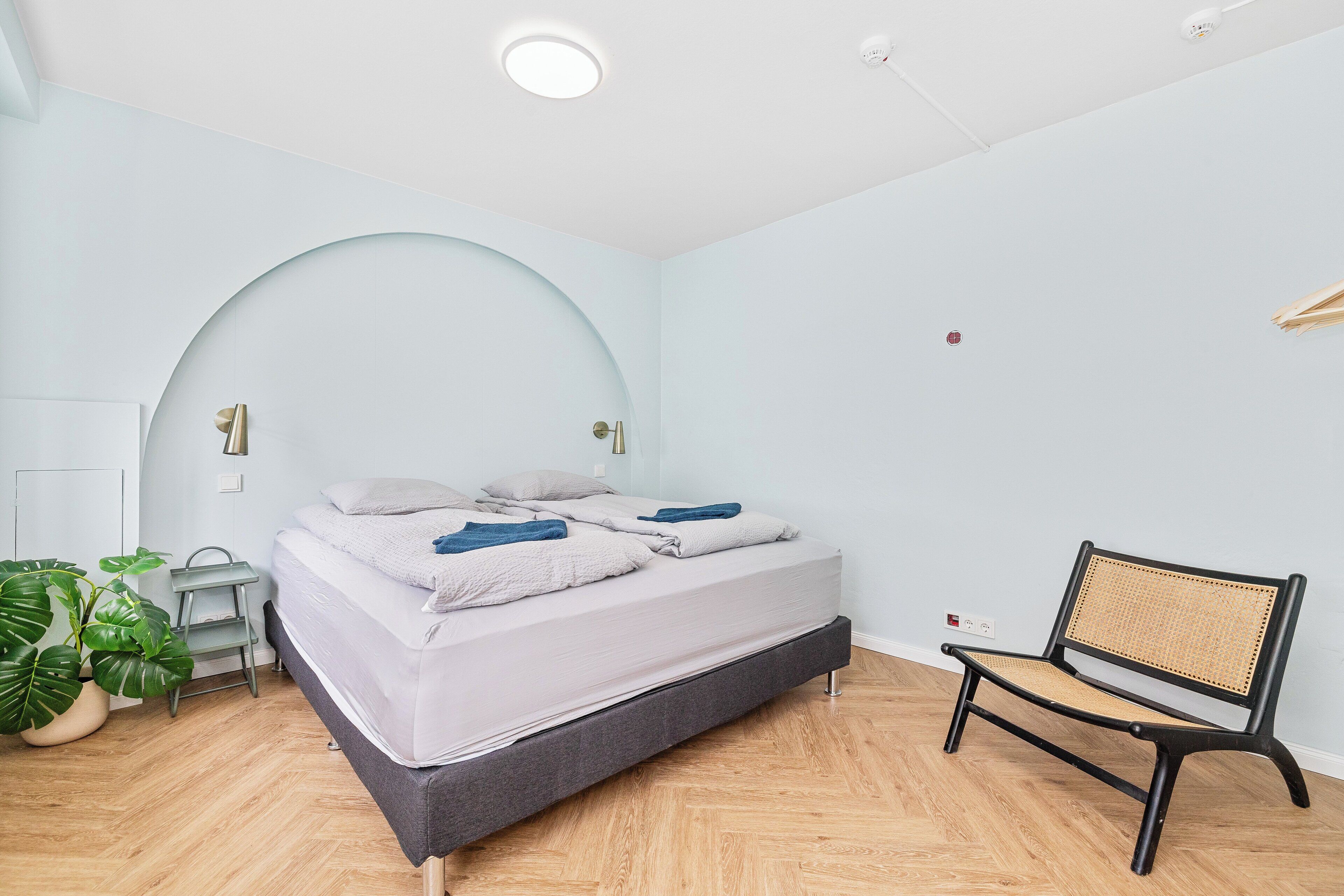 A bedroom with a bed, bedside tables, a chair, and a potted plant.