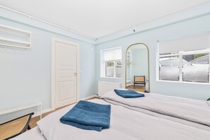 Een kamer met twee bedden, een witte deur, een raam met uitzicht op geparkeerde auto's en een spiegel aan de muur.
