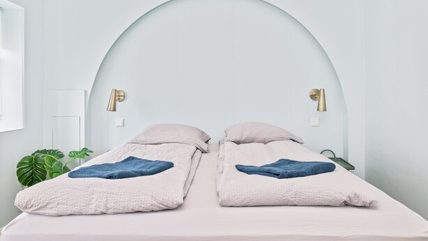 Ein Zimmer mit zwei Betten, jeweils mit blauem Handtuch und weißer, strukturierter Decke.