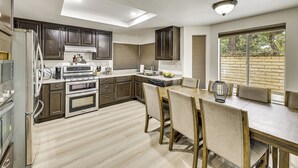 A modern kitchen with dark wood cabinets, stainless steel appliances, and a dining area with a wooden table and chairs. - 2 Mi to Victoria Gardens: Rancho Cucamonga Haven (Rancho Cucamonga)