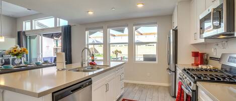 A modern kitchen with a dishwasher, stove, refrigerator, and large windows.