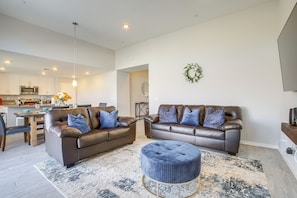 A modern living room with two brown leather sofas, a round ottoman, and a dining area with a wooden table and chairs.
