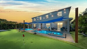 A modern two-story house with a swimming pool, a covered patio, and a well-maintained lawn.