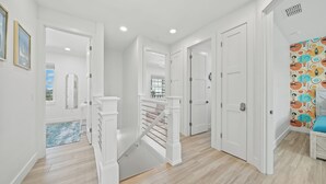 A modern hallway with white walls, wooden flooring, and a staircase with white railings.