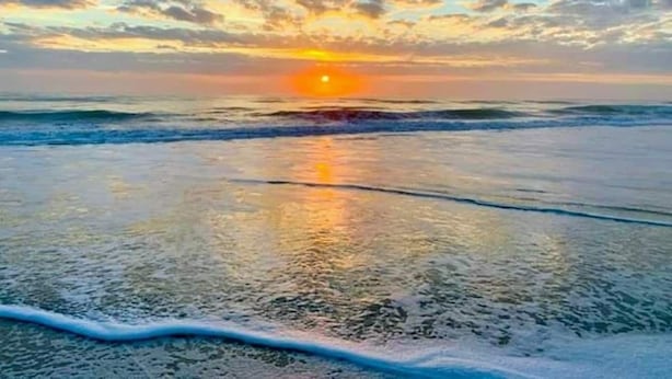 A beach with a sunset, waves, and a clear sky.