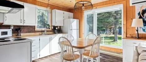 A modern kitchen with white cabinets, a dining table with chairs, and a large window offering a view of trees.