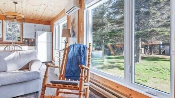 Una habitación acogedora con un amplio ventanal, una mecedora de madera y un sofá blanco.