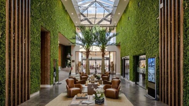 Eine geräumige Lobby mit hoher Decke, Wandverkleidungen in Grün und einer zentralen Sitzecke mit Ledersesseln und einem Couchtisch.