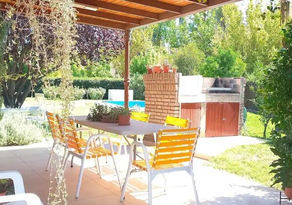 An outdoor patio with a table and chairs, surrounded by greenery and a brick structure.