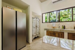 Una cocina con refrigerador, ventana con vista a vegetación y muebles de madera.