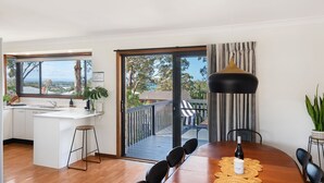 Une cuisine moderne avec une grande fenêtre, un coin repas avec une table et des chaises en bois, et un balcon avec vue.