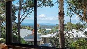 Une vue depuis une fenêtre donnant sur un quartier résidentiel, avec des maisons, des arbres et un paysage lointain.
