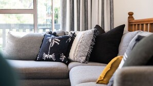 Un canapé modulable avec plusieurs coussins, une tête de lit en bois et une vue sur un balcon par une fenêtre.