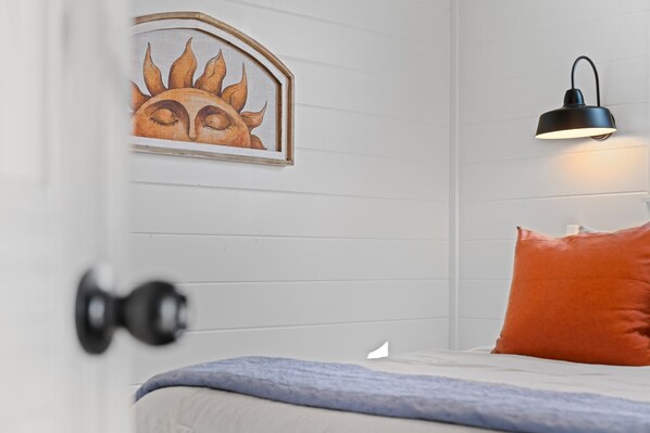 A bedroom with a bed, a wall-mounted lamp, and a framed artwork. - Chin 2 (Fredericksburg)