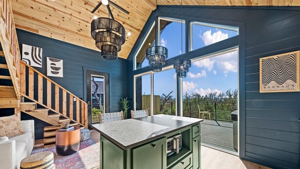 Une cuisine moderne dotée d’un îlot central, d’un escalier en bois et de grandes fenêtres.