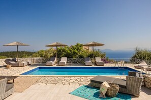 A pool area with lounge chairs, umbrellas, and a view of the sea. - Villa Renata. (Katsarata)
