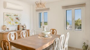 A dining area with a wooden table, white chairs, a decorative bowl centerpiece, and a painting on the wall. - Villa Renata. (Katsarata)