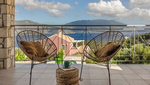 Two wicker chairs with cushions on a balcony overlooking a scenic view of mountains and a body of water. - Villa Renata. (Katsarata)