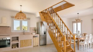 A spacious kitchen with a wooden staircase, a dining area, and a view of the outdoors. - Villa Renata. (Katsarata)