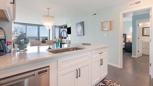 A modern kitchen with a large island, white cabinetry, and a chandelier. - Oceanfront Lux at Palms Resort Views and Amenities (Myrtle Beach)