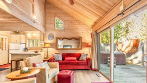 Interior acogedor de una cabaña con cocina, un sofá rojo y un amplio ventanal corredero que da a una terraza exterior.