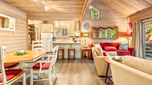 Interior acogedor de una cabaña con una mesa de comedor de madera, sillas con cojines rojos, un sofá rojo y una cocina con fregadero y estufa.