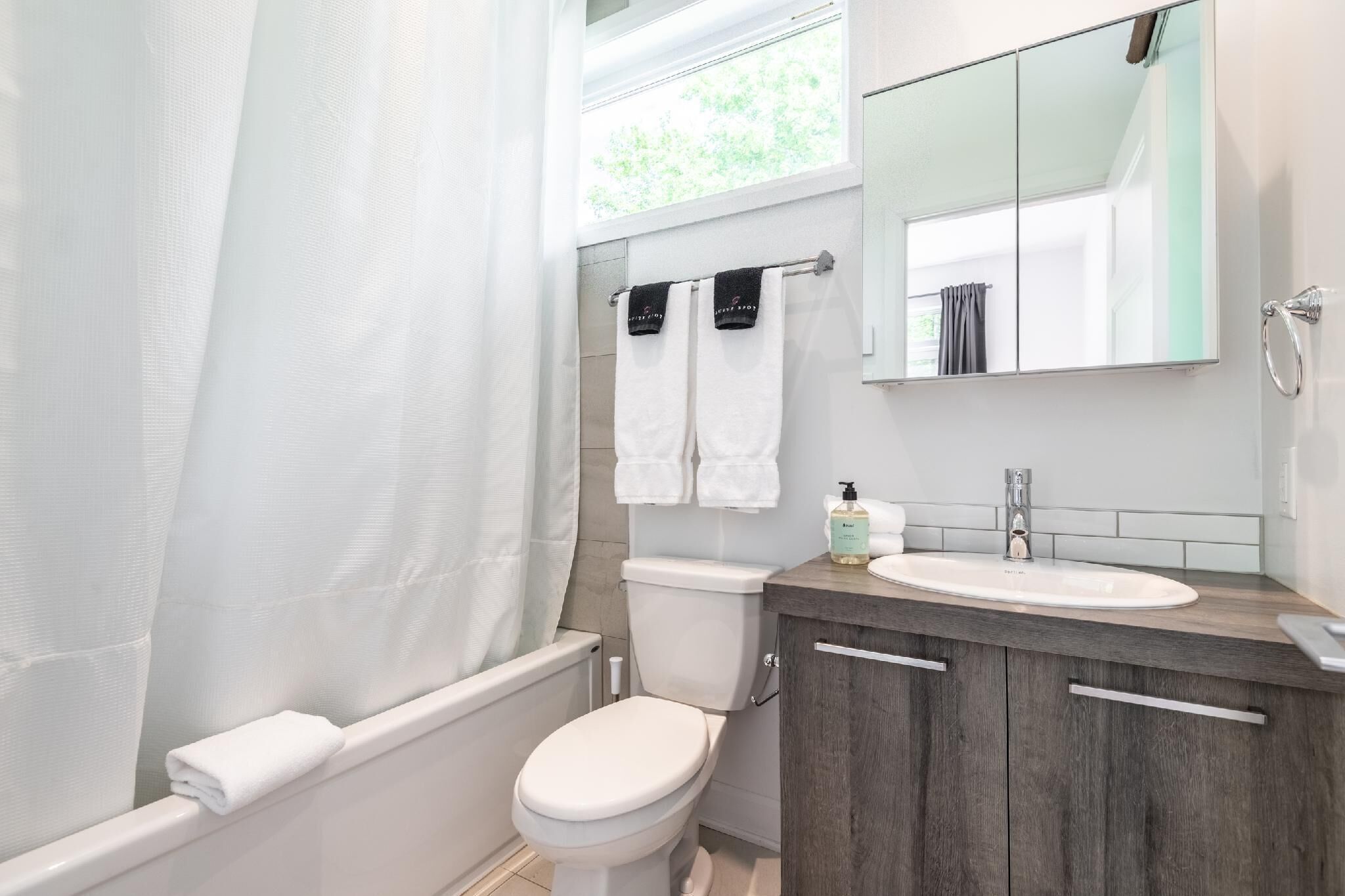 Une salle de bain avec des toilettes blanches, un lavabo avec un miroir au-dessus et un rideau de douche.