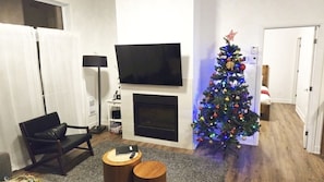 A living room with a fireplace, a TV mounted above it, a Christmas tree, and a black leather chair.
