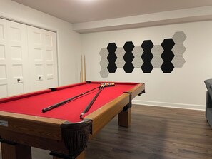 A pool table with a red felt surface, surrounded by wooden legs and a black cloth.