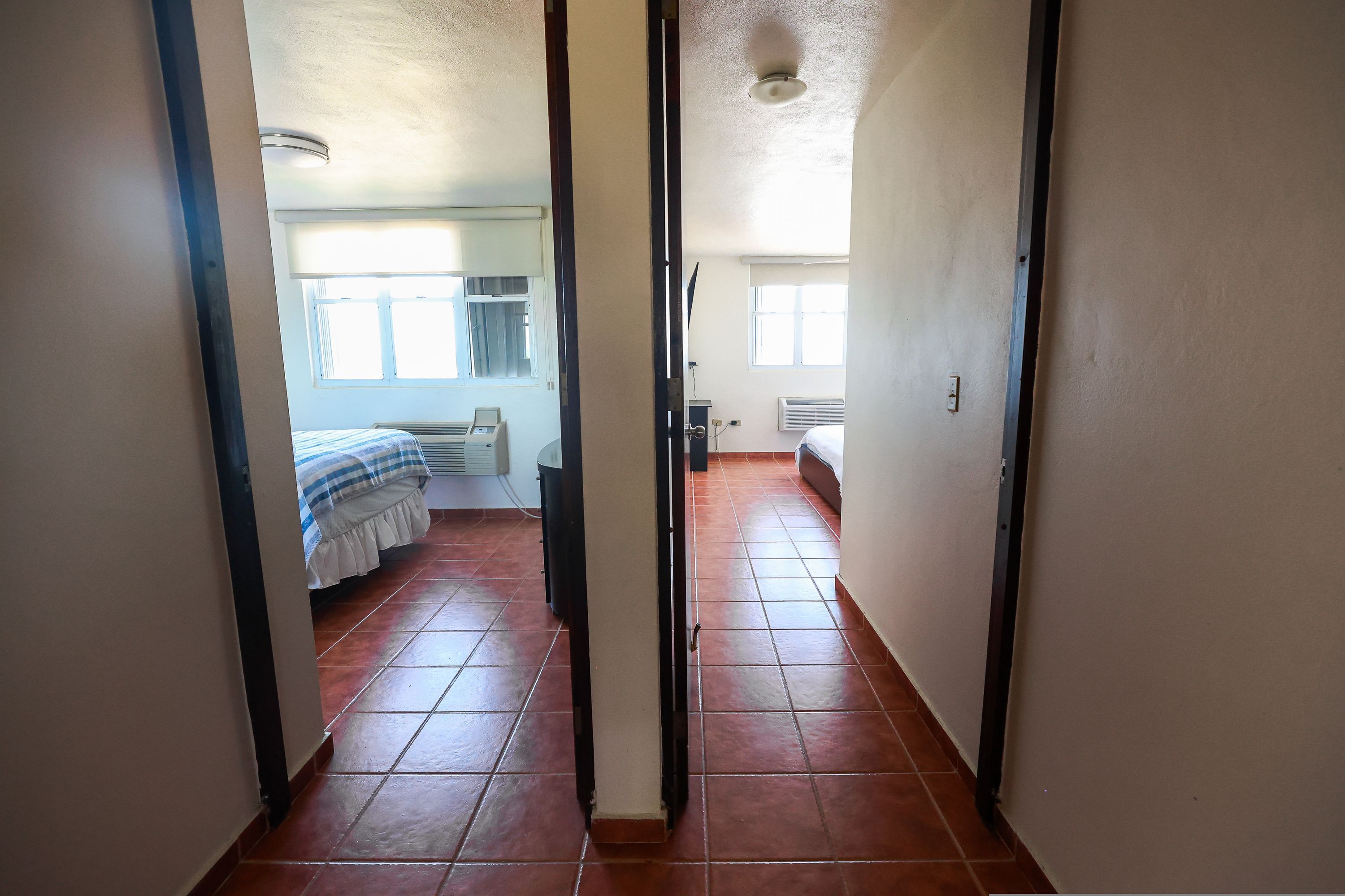 Ein Flur, der in ein Schlafzimmer mit Bett, Fenster und Heizkörper führt.