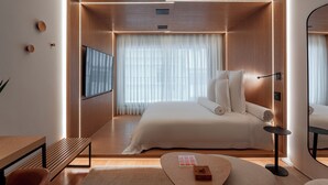 Ein modernes Hotelzimmer mit einem großen Bett, einem Flachbildfernseher, einer Holzbank und einem kleinen Tisch.