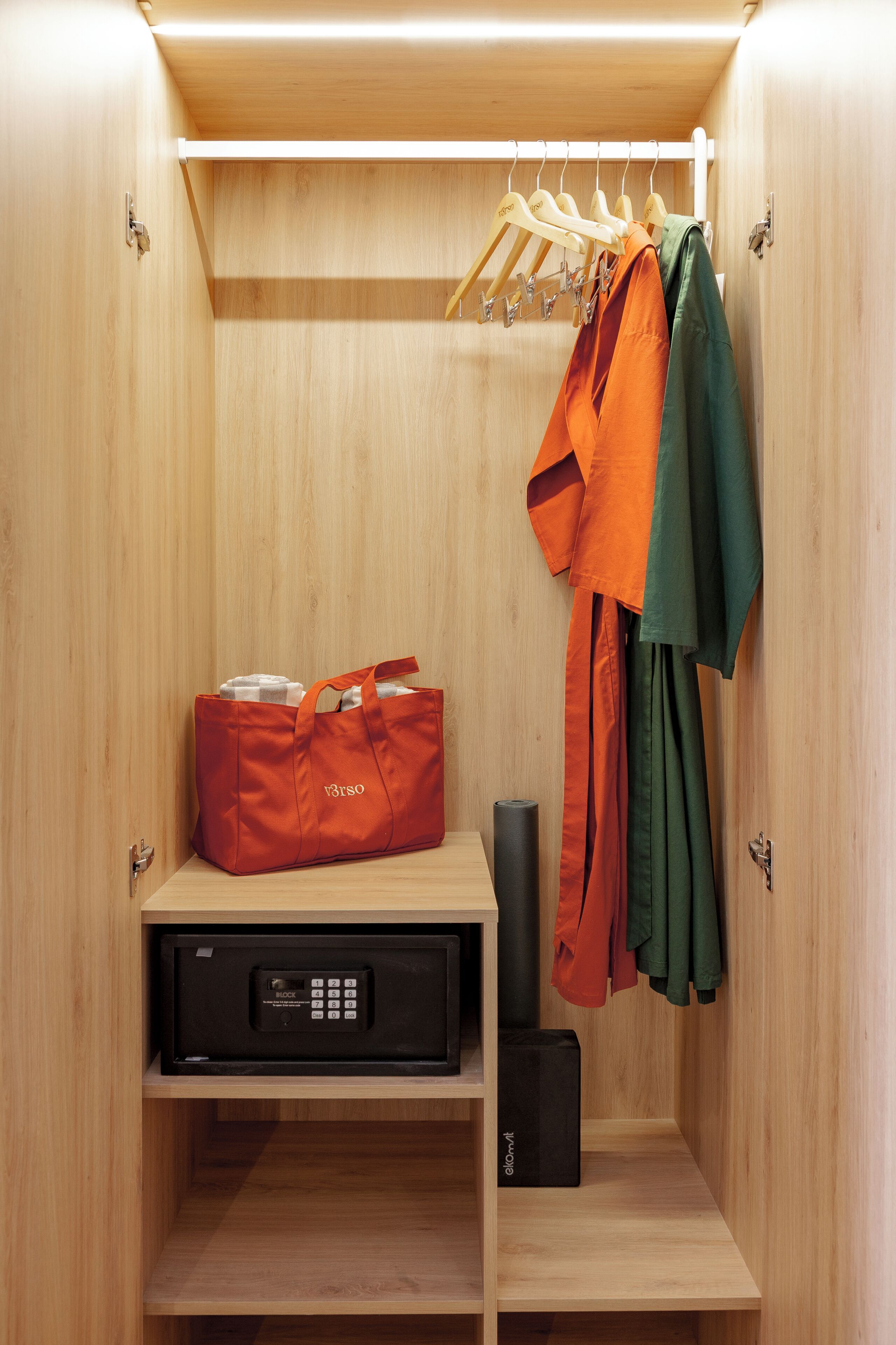A wooden wardrobe with hanging clothes, a red bag, and a black electronic device.