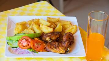 A plate of food with fries, chicken, and vegetables, and a glass of orange juice on a yellow checkered tablecloth.