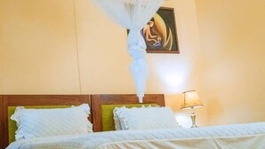 A hotel room with a bed, a nightstand with a lamp, and a painting on the wall. - Bethany Hotel Karongi (Bwishyura)