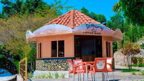 A small, single-story building with a tiled roof and a sign that reads "Bethany Coffee Shop." In front of the building, there are several orange plastic chairs and a hammock. - Bethany Hotel Karongi (Bwishyura)