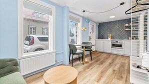 A modern kitchen with white cabinets, a dining area with a round table and chairs, and a large window overlooking a street. - Central studio apartment (Reykjavik)