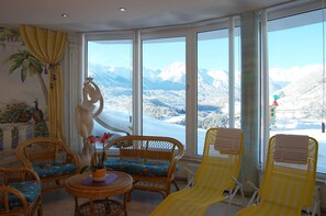 A room with large windows offering a mountain view, wicker furniture, and a statue. - Apartment in Pitztal With Mountain Views (Arzl im Piztal)