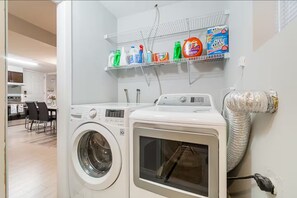 Uma área de lavanderia com máquina de lavar, secadora e prateleiras com produtos de limpeza.