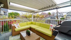 Ein überdachter Außenbereich mit einer grünen Couch, einem kleinen Tisch mit einer Pflanze und einem Grill.