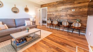 Un salon moderne avec un mur d’accent en bois, un canapé, une table basse et un coin repas avec des chaises.