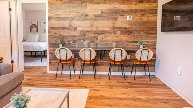 Un coin repas avec un mur en bois, quatre chaises en osier et une table.
