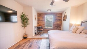 Une chambre à coucher avec un lit, une petite table, une chaise, une plante en pot et une fenêtre.
