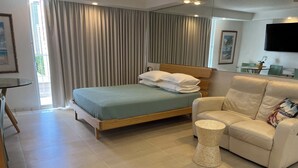 Een moderne hotelkamer met een bed, een slaapbank, een klein rond tafeltje en een aan de muur bevestigde televisie.